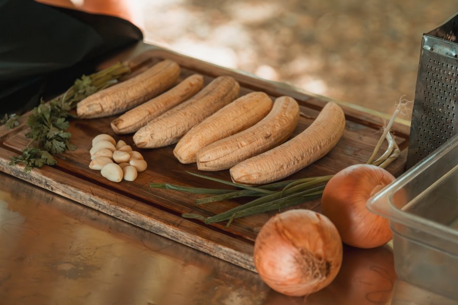 A cutting board holding peeled plantain, garlic, cilantro, and onions to make cream of plantain soup.