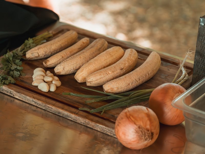 A cutting board holding peeled plantain, garlic, cilantro, and onions to make cream of plantain soup.